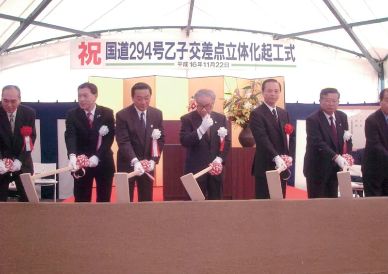 「祝 国道294号乙子交差点立体化起工式」の看板の前で鍬入れをする関係者